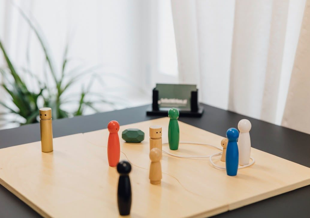 Bunte Holzfiguren und ein grüner Stein auf einem hellen Holzbrett