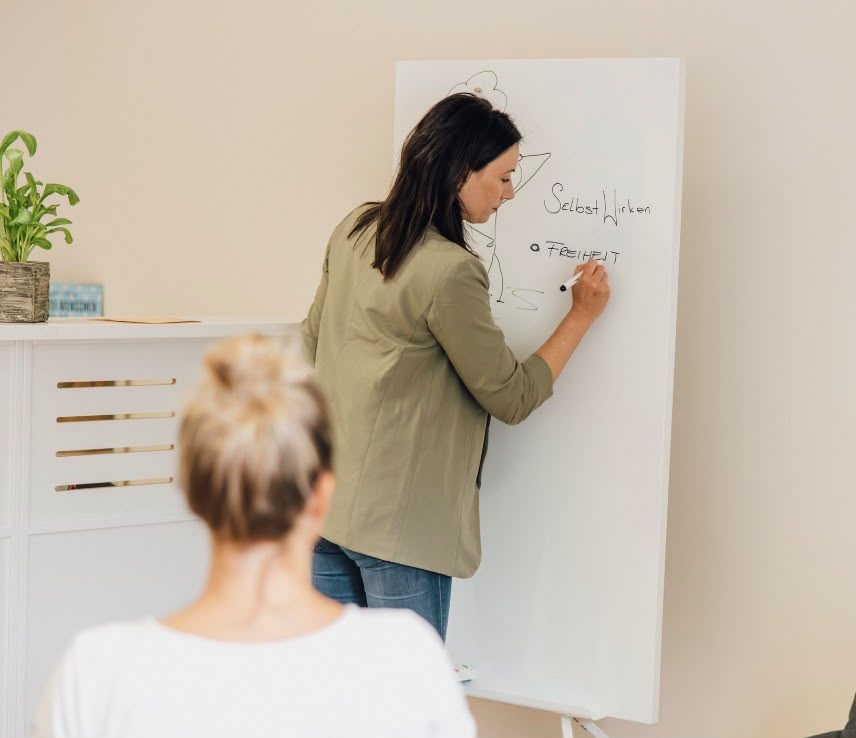 Eine Frau schreibt „Freiheit“ auf ein Whiteboard, im Vordergrund hört eine Person zu